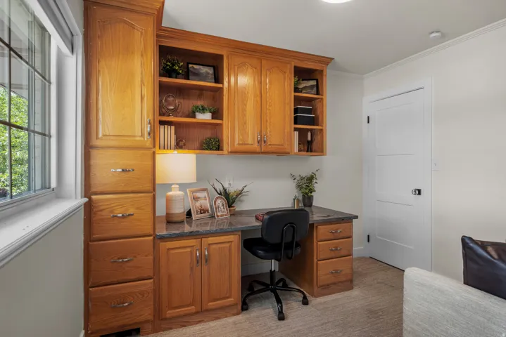 Built-in wood cabinetry with a dark speckled countertop, integrated desk, and open shelving