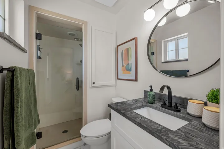 Bathroom featuring a glass-enclosed shower, single vanity with dark countertop, undermount sink, and matte black faucet