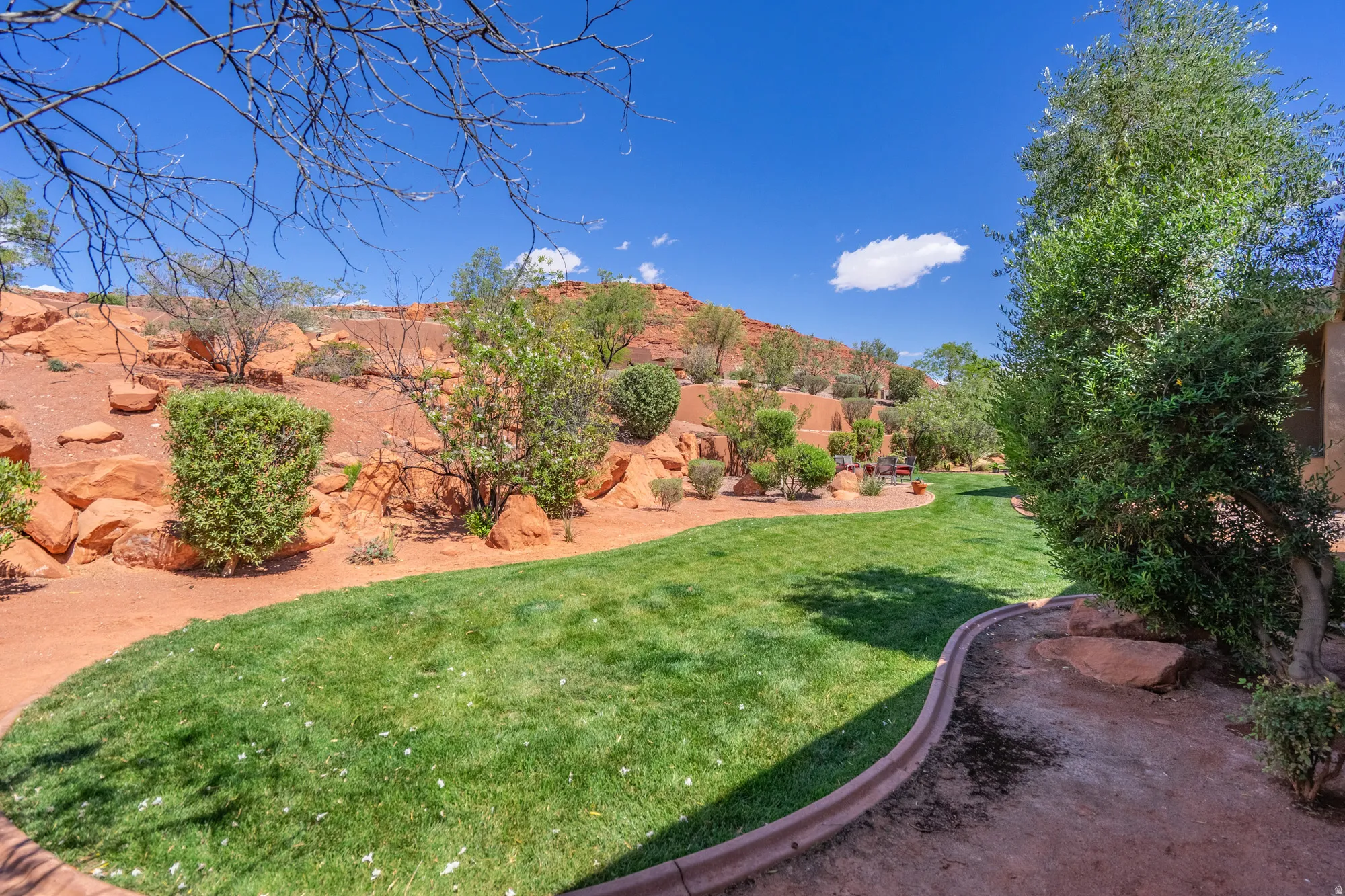 Expansive lawn area with a decorative border, surrounded by red rock landscaping