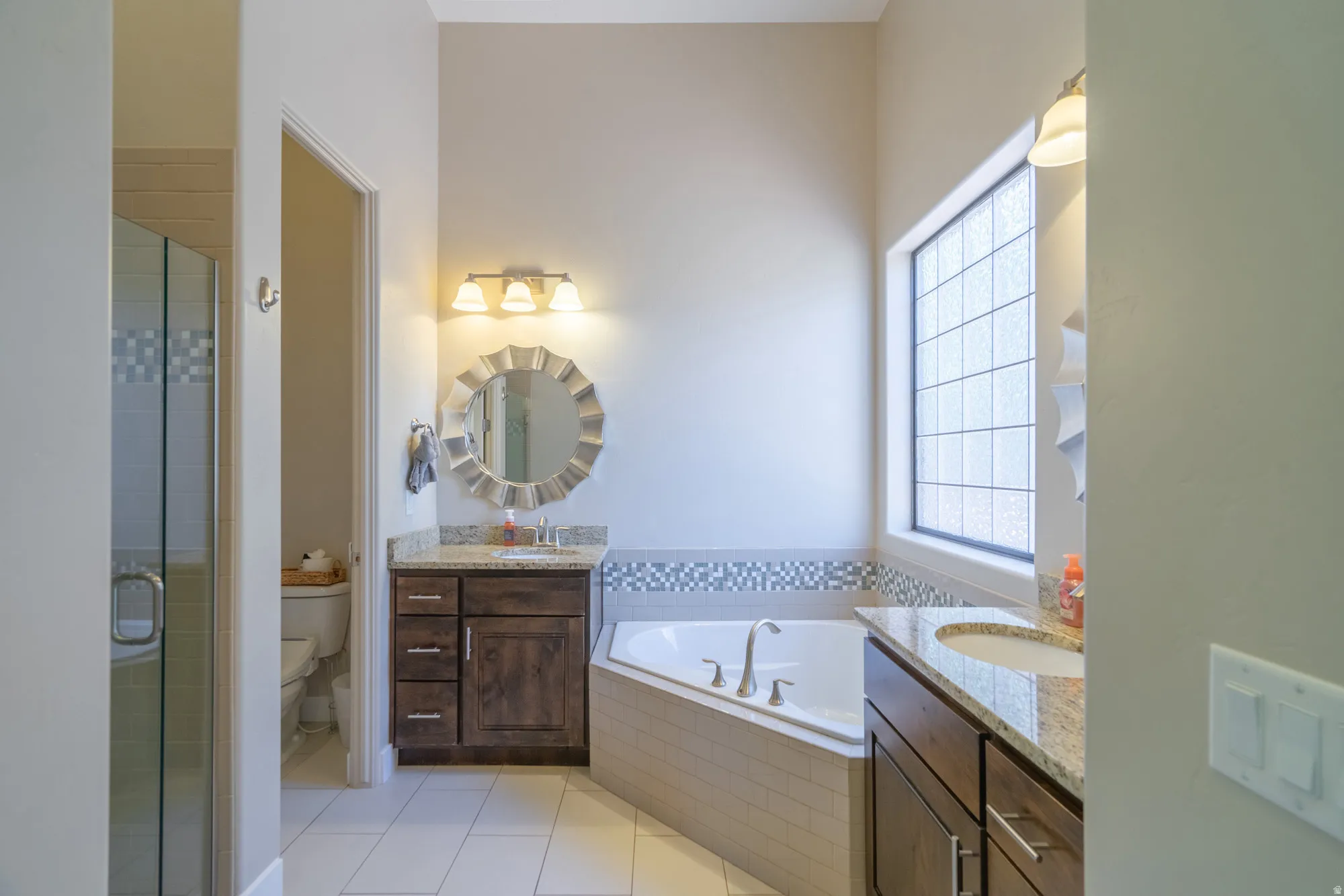 Bathroom featuring a corner soaking tub with tile surround, dual vanities with granite countertops, and wood-finish cabinetry