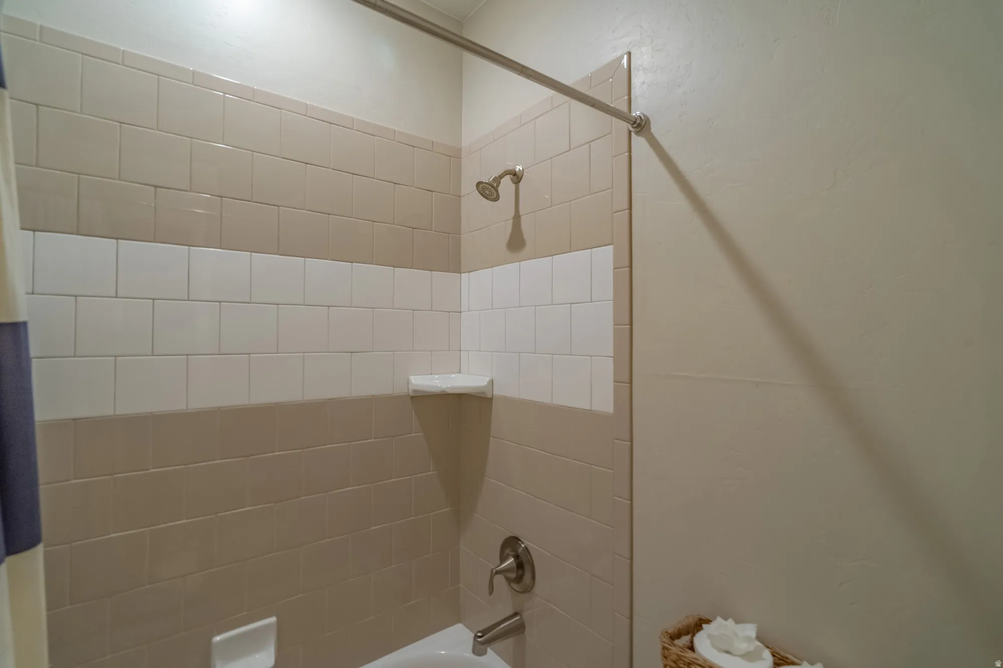 Bathtub shower combination with two-tone tiled surround, brushed nickel fixtures, and wall-mounted shower head