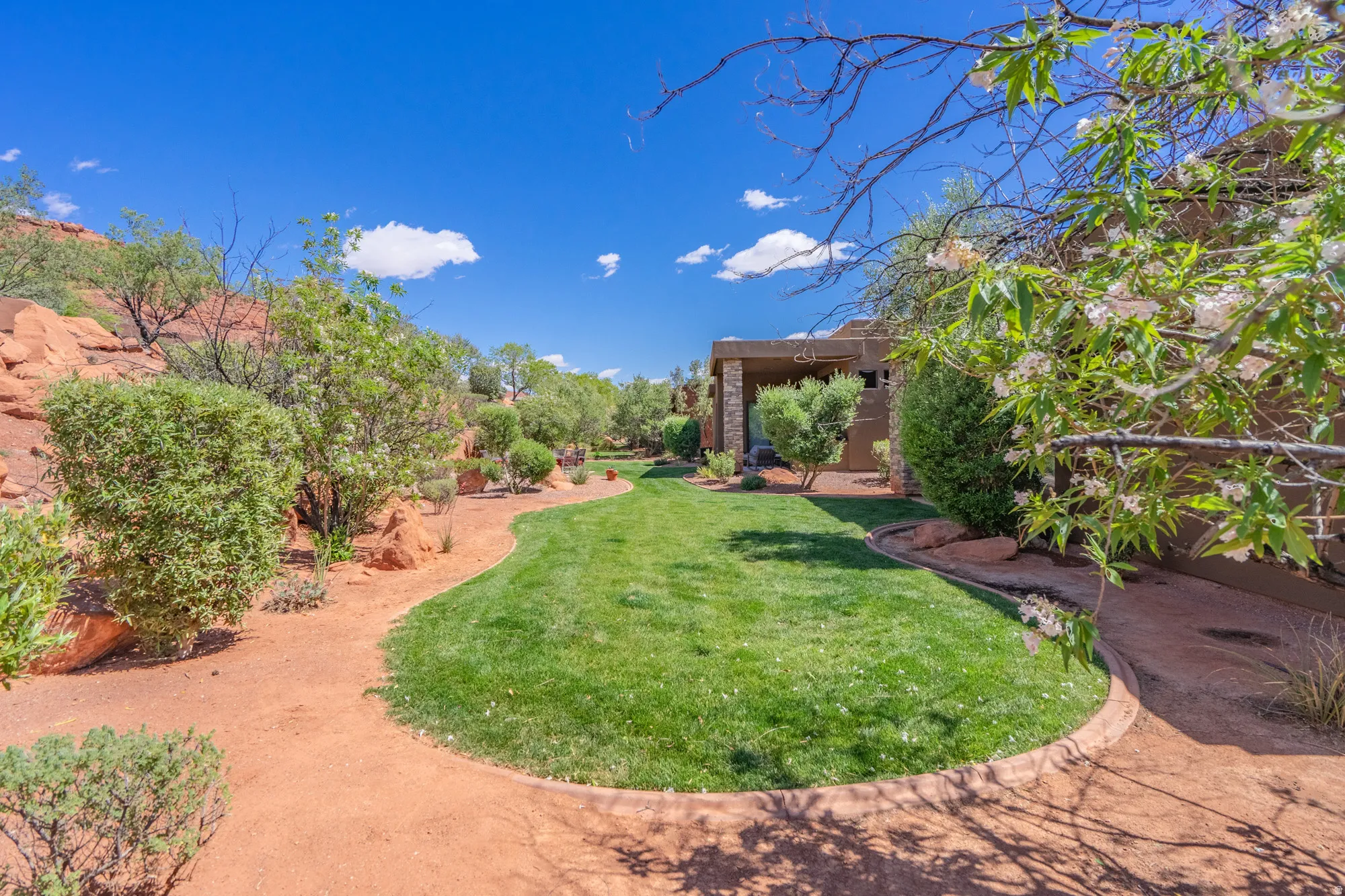 Expansive green lawn bordered by a sculpted pathway, arid landscaping, and a stucco exterior