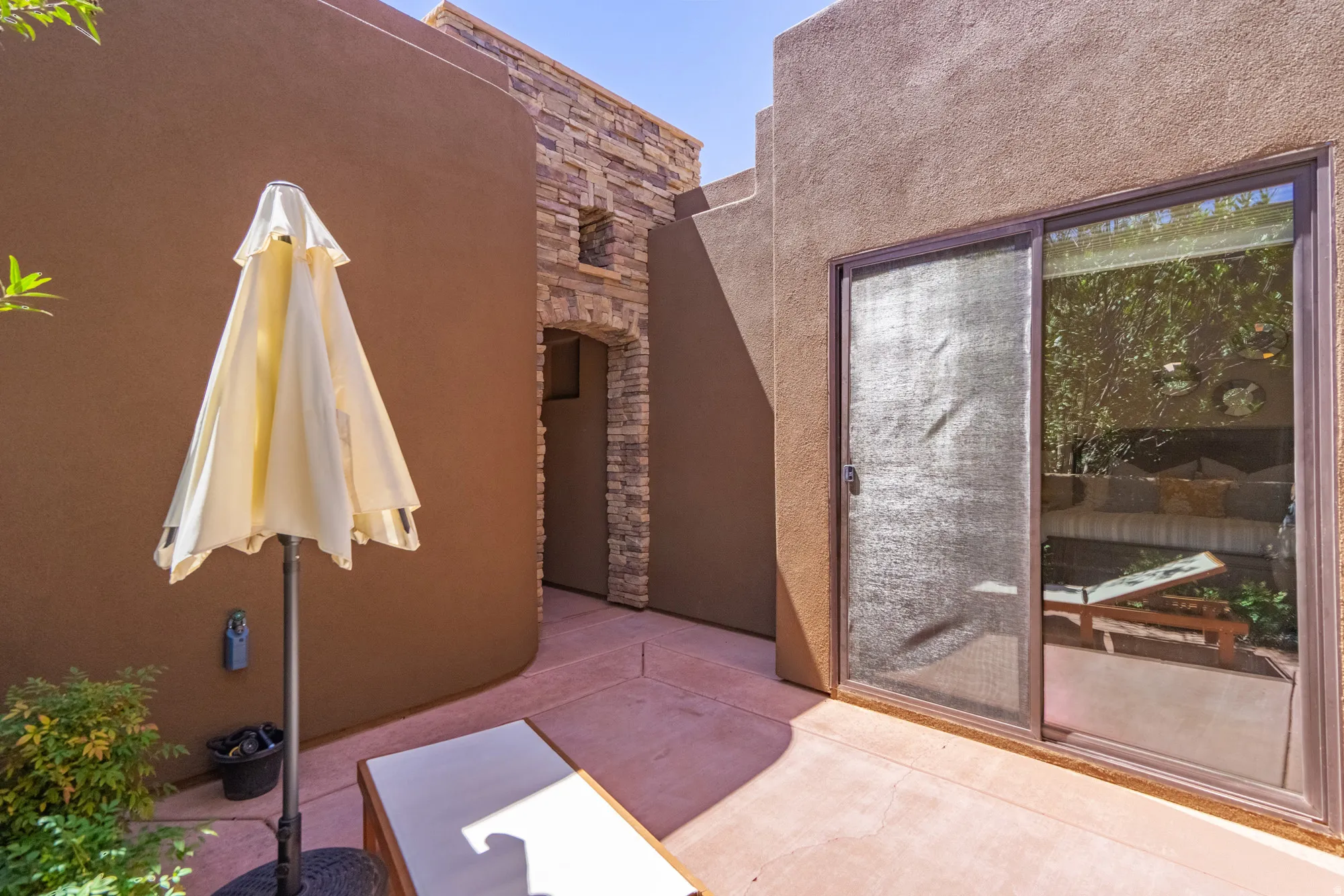 Exterior patio area featuring earth-toned stucco walls, a stone-accented arched entryway, and a sliding glass door with an integrated screen