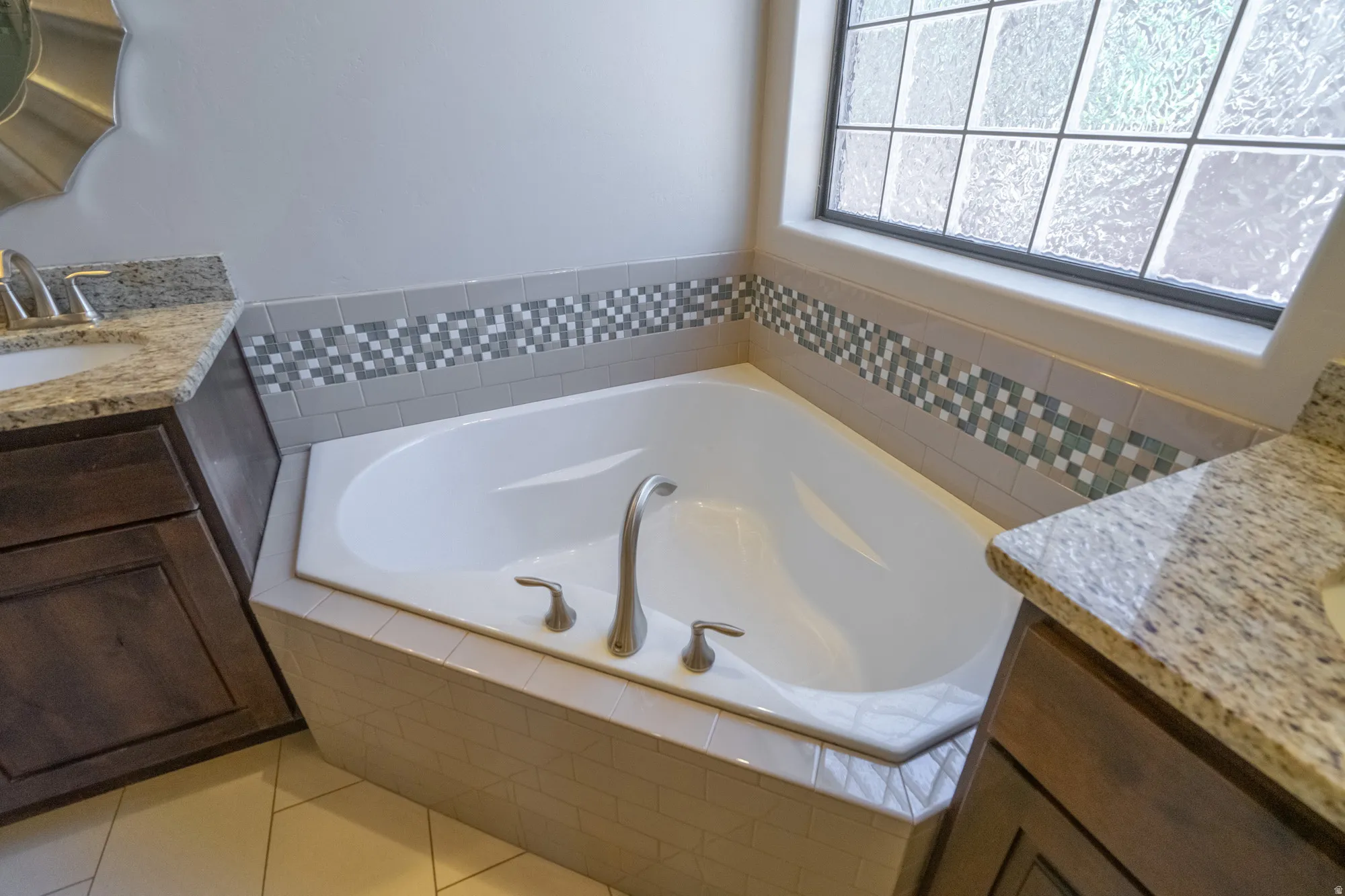 Corner soaking tub featuring a decorative tile surround and textured glass window