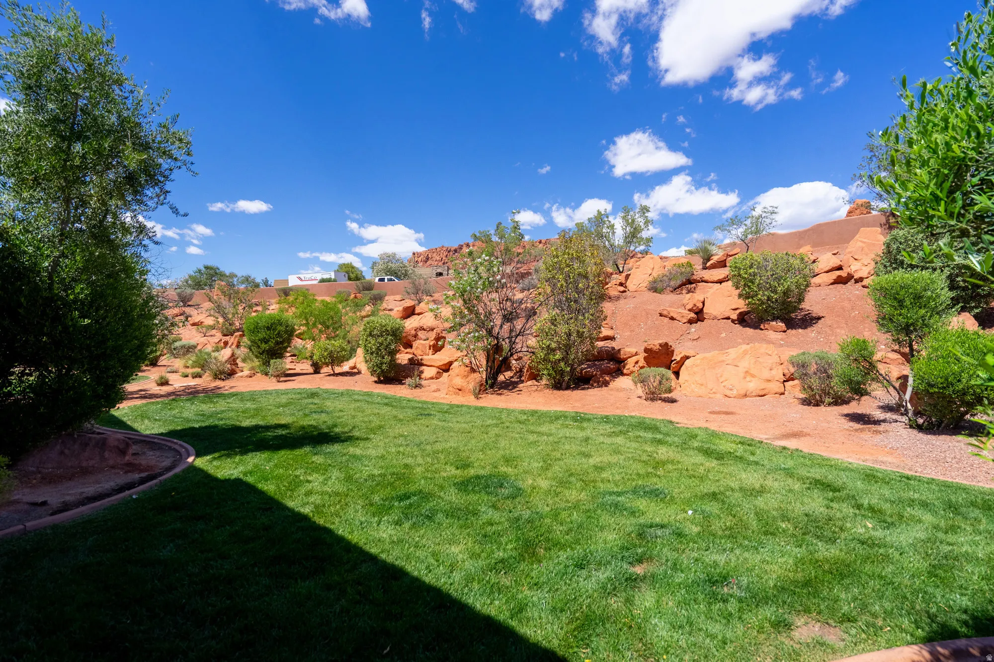 Expansive backyard featuring a lush green lawn, mature landscaping, and a red rock natural hillside