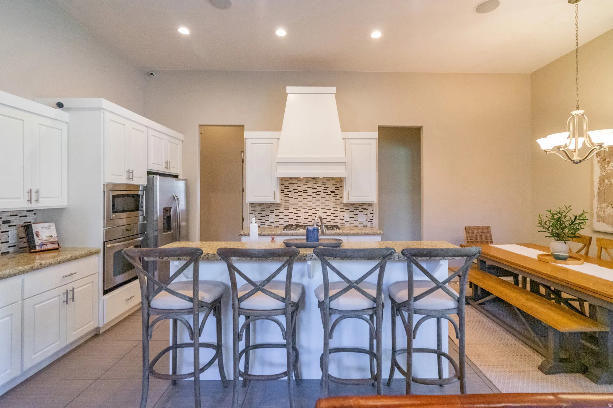 Open-concept kitchen featuring white shaker cabinetry, stainless steel appliances, granite countertops, and a patterned tile backsplash