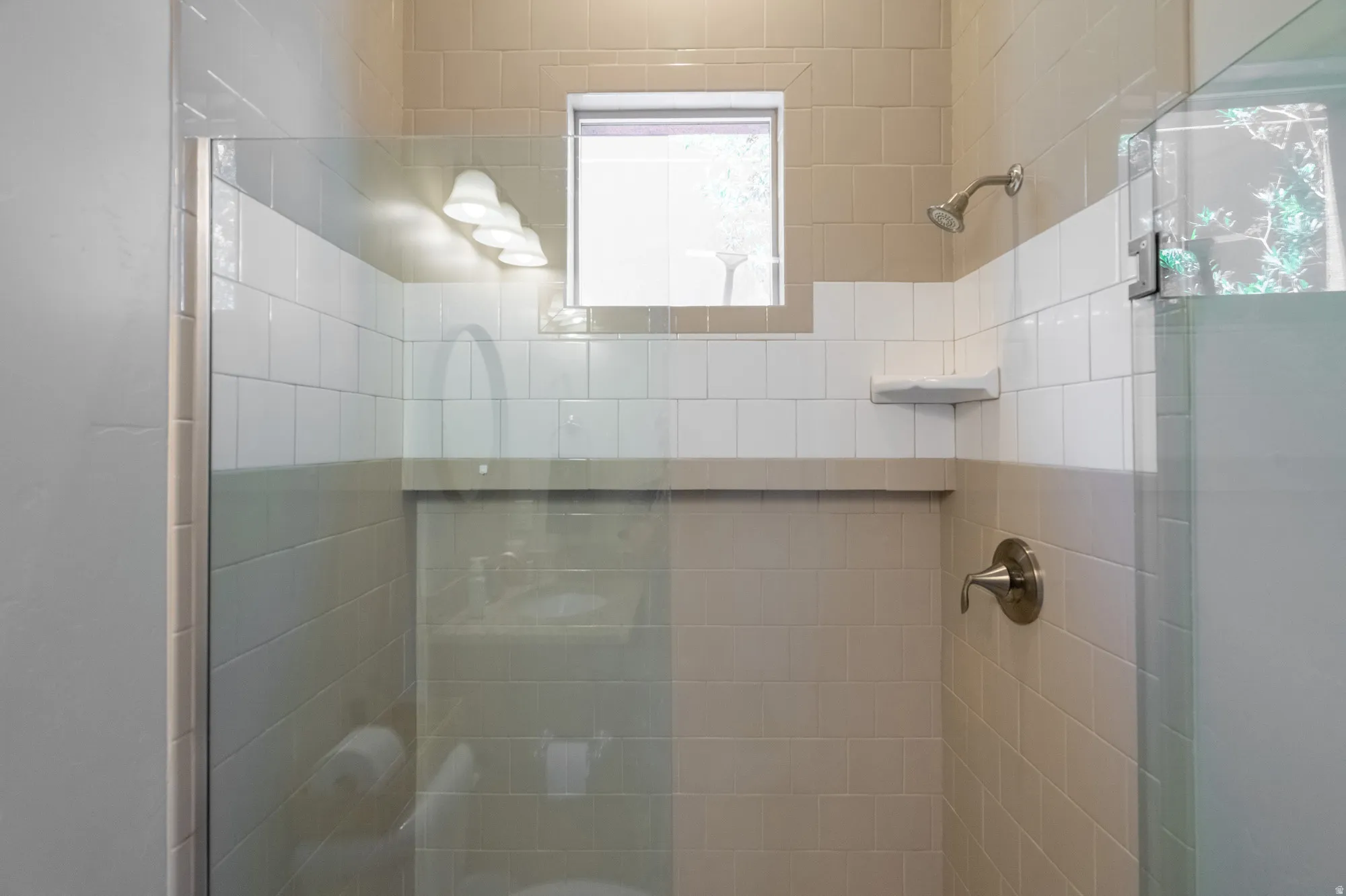 Glass-enclosed shower with a tiled surround, featuring a built-in shower niche, a window, and a brushed nickel showerhead and faucet