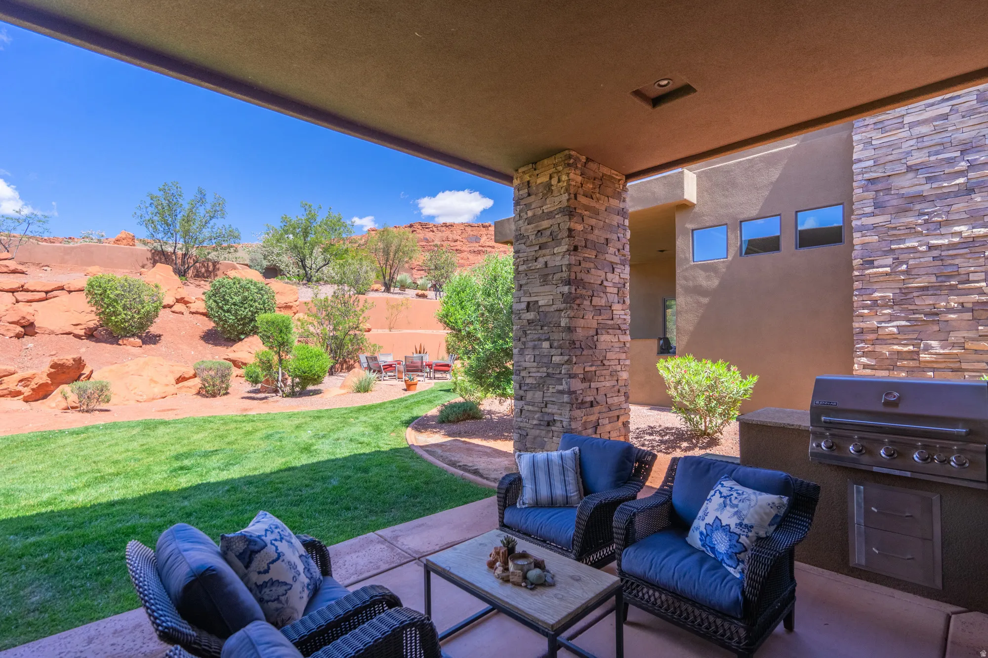 Covered patio featuring a built-in outdoor kitchen with grill, stone veneer accent walls and columns, concrete flooring, and a manicured lawn