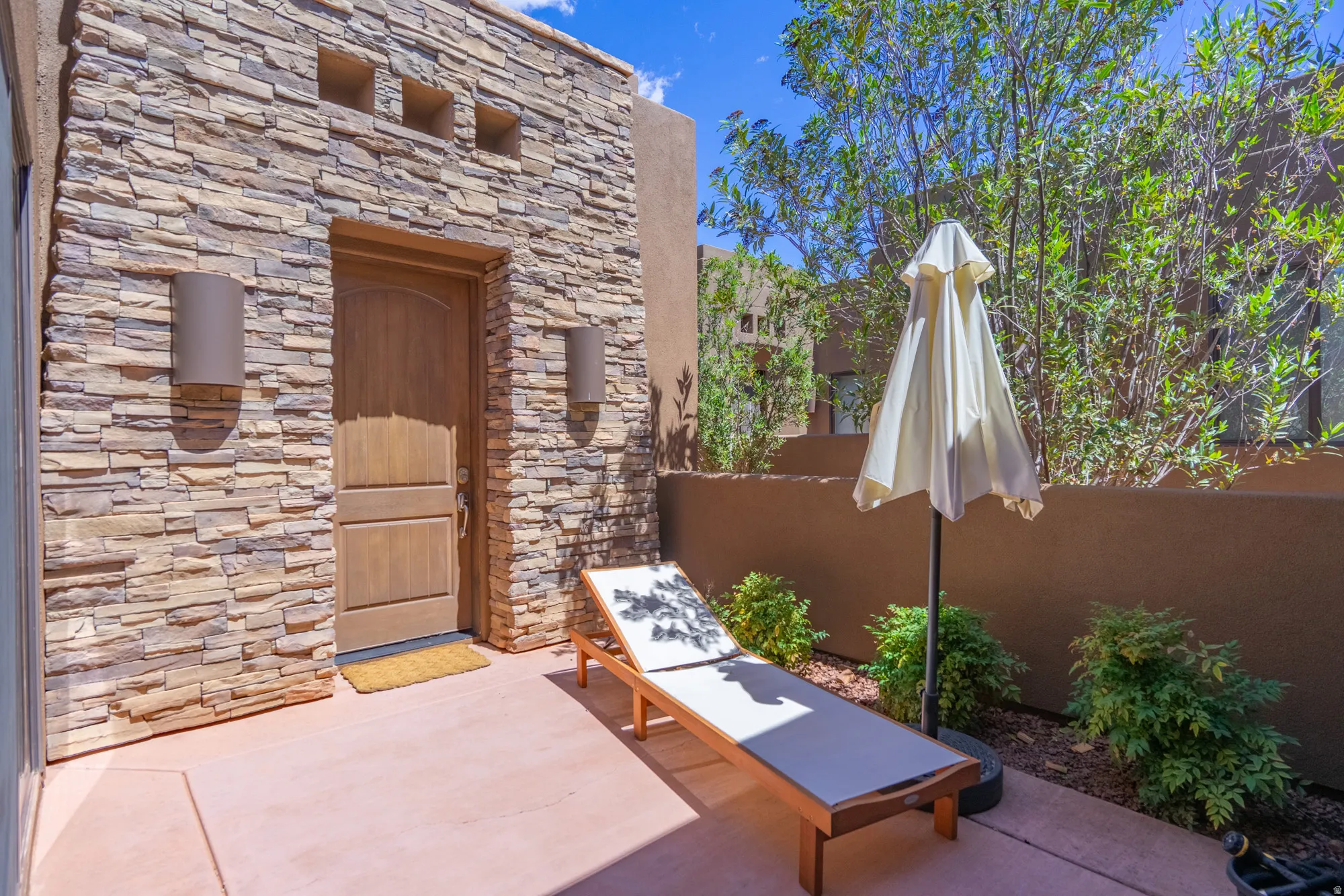 Private outdoor patio area featuring a textured stucco wall and stacked stone facade