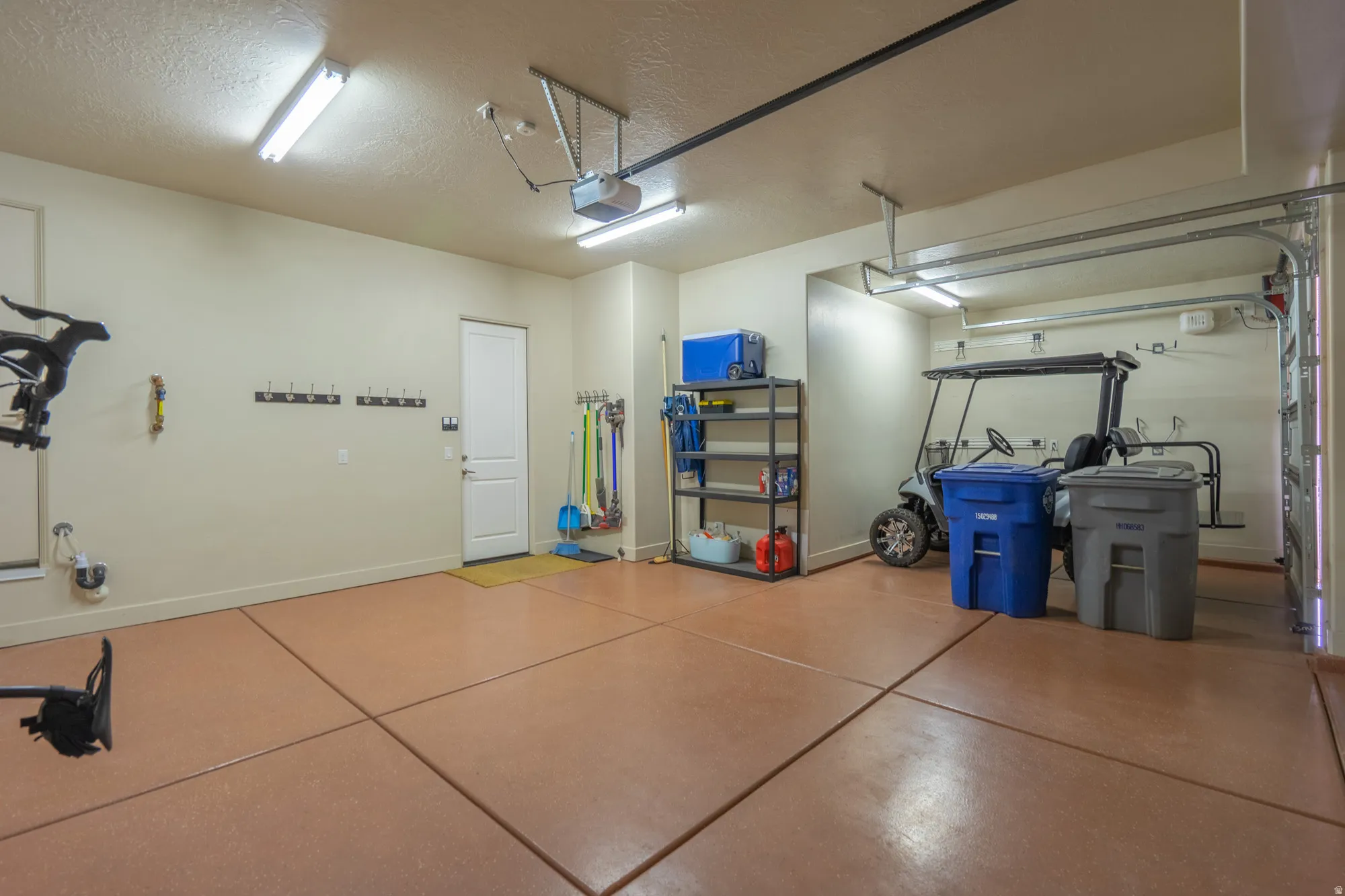 Spacious garage featuring a durable epoxy-coated concrete floor, bright overhead fluorescent lighting, and a white interior door