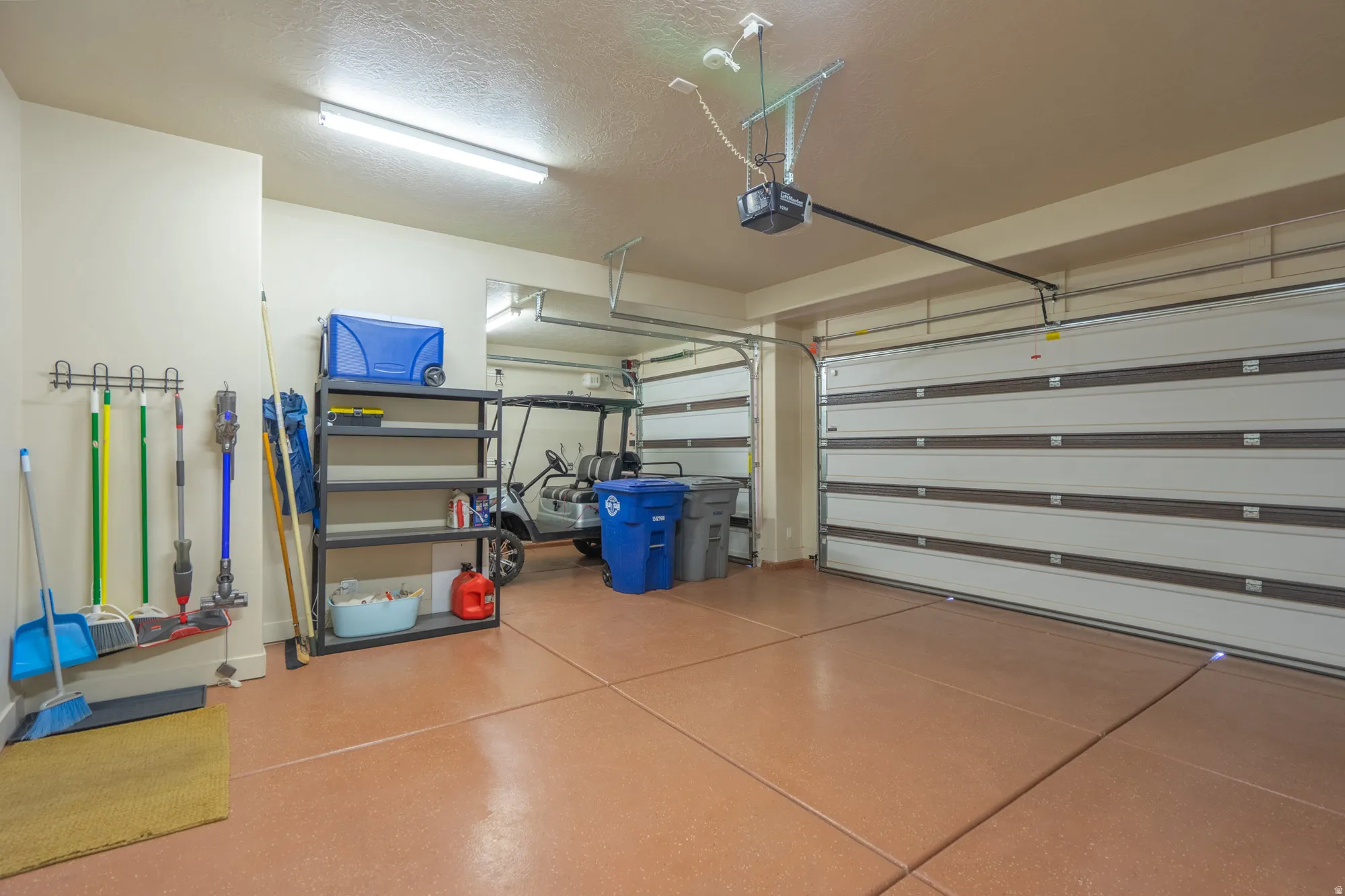Spacious garage featuring two overhead doors, an automatic opener, a light brown finished concrete floor, and fluorescent ceiling lighting