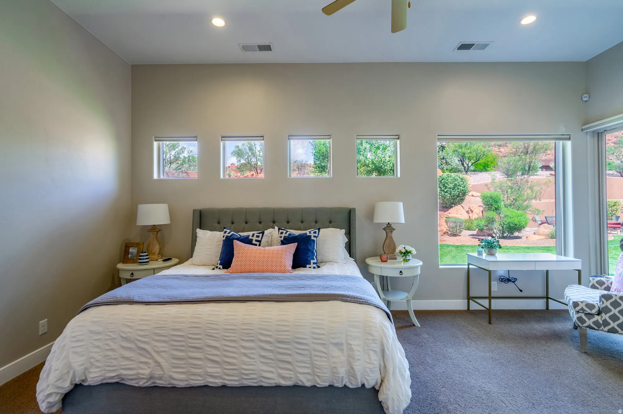Carpeted room featuring a large window overlooking a landscaped outdoor space, three smaller square windows, recessed lighting, and a ceiling fan