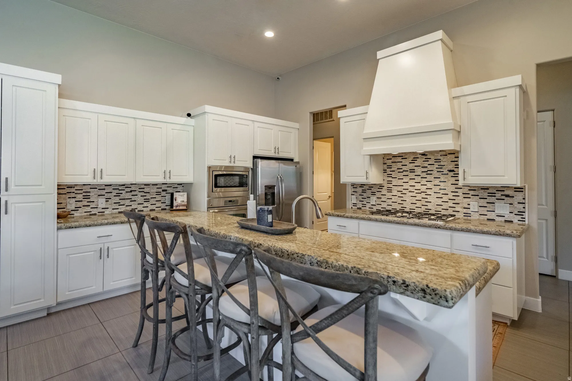 Kitchen featuring an expansive island with a granite countertop, white cabinetry, a decorative range hood, and a mosaic tile backsplash