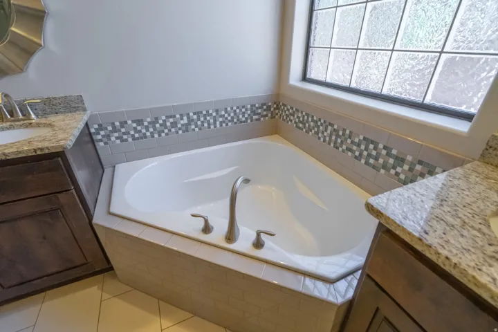 Corner soaking tub featuring a decorative tile surround and textured glass window
