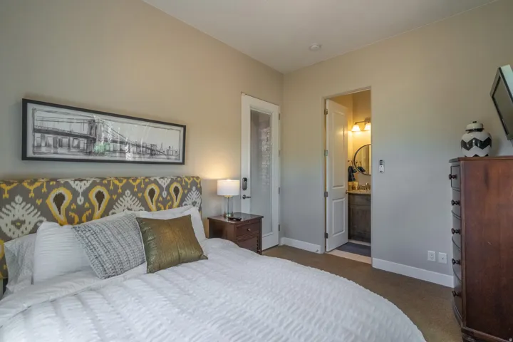 Neutral-toned bedroom featuring carpeted flooring and an adjacent bathroom with a vanity and circular mirror