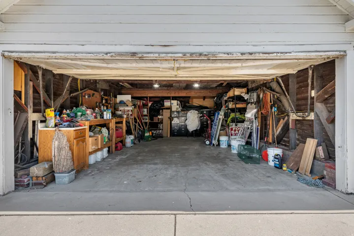 Attached two-car garage with concrete flooring, exposed wooden beams, and interior lighting