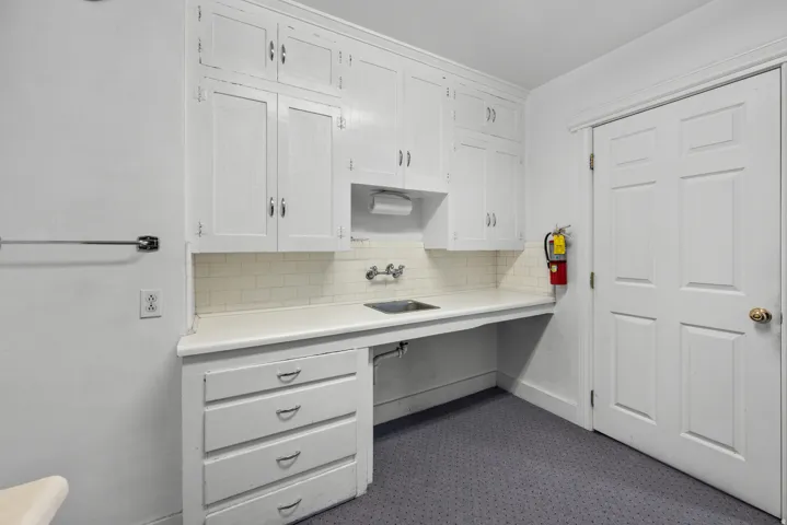 Functional workspace featuring white cabinetry, a built-in sink, white countertop, and subway tile backsplash