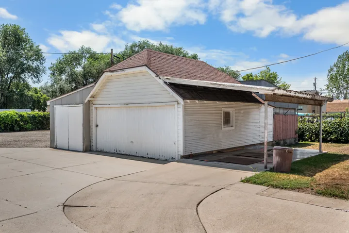 Detached garage structure with a single garage door, an additional storage door, and an attached carport