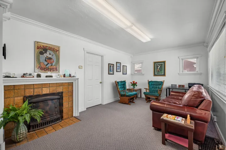 Carpeted room featuring a tiled fireplace with an ornate iron insert, multiple windows with blinds, a white paneled door, and crown molding