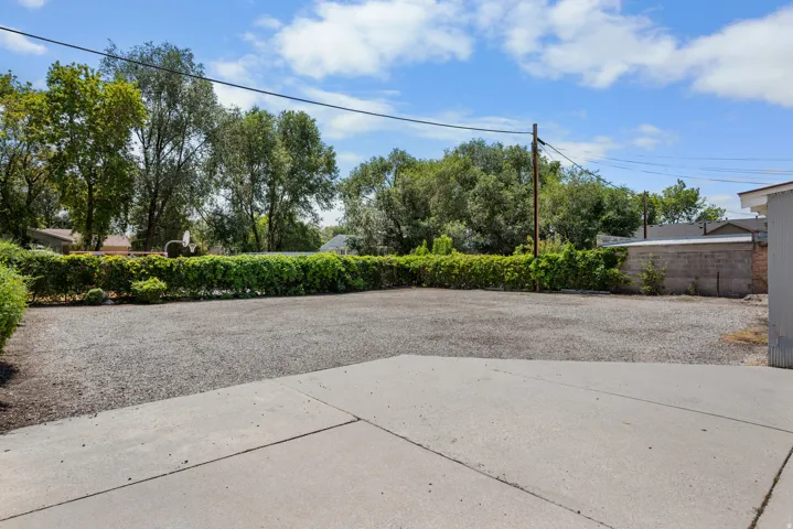 Expansive gravel area with concrete pad, surrounded by mature trees and a manicured hedge