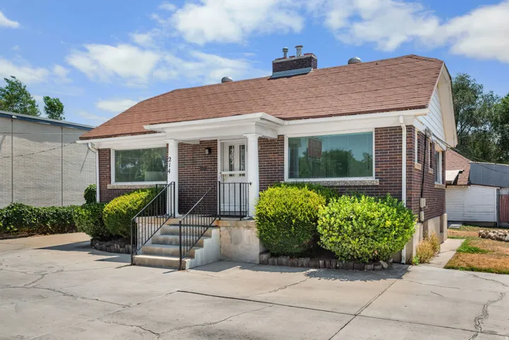 Brick exterior with a brown shingle roof, featuring white trim, a front porch with white columns, and wrought iron railings leading to the entrance