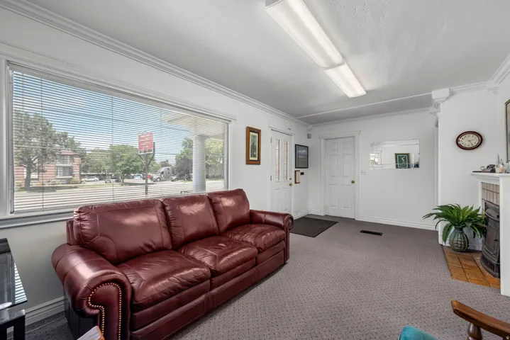Spacious reception area featuring a large window with horizontal blinds, neutral carpeting, and crown molding
