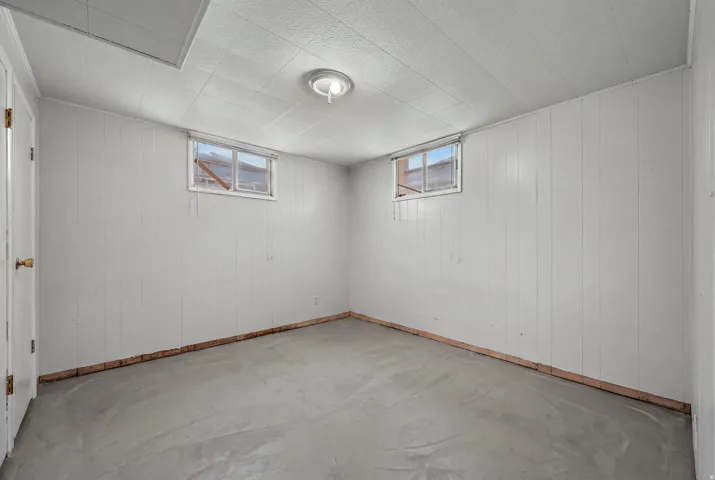 Room featuring light-colored vertical paneling, a suspended ceiling, and two windows