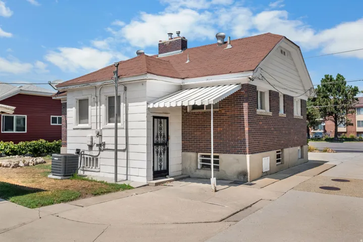 Rear exterior featuring a brick and white siding facade, a red shingle roof, a sheltered entryway with an awning, and a paved concrete surface