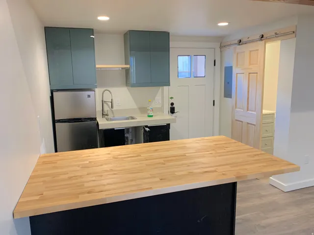 Compact kitchen space featuring a butcher block countertop, stainless steel refrigerator, and teal overhead cabinetry
