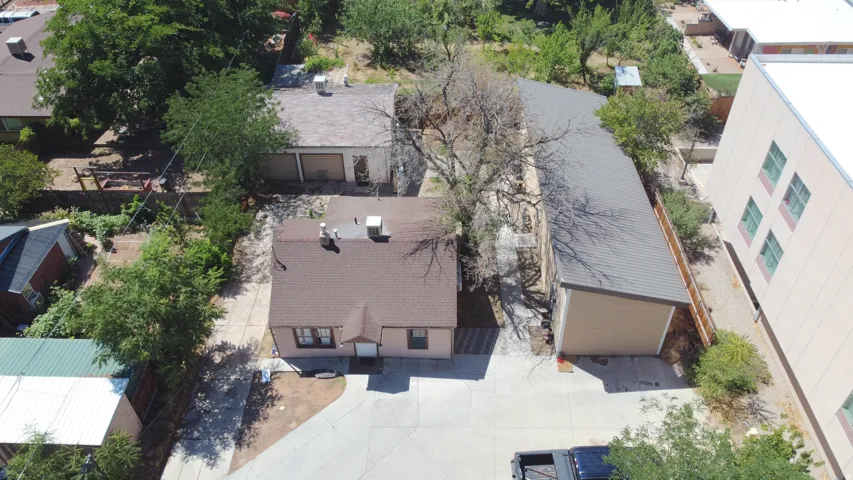 Aerial property perspective featuring a main residence with a brown shingle roof, a detached garage structure with a gray metal roof, and a separate outbuilding with a flat roof