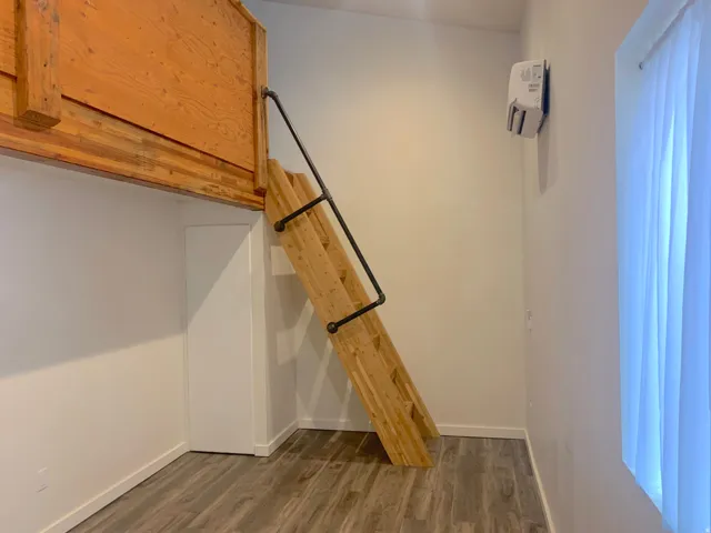 Lofted wood-finish sleeping area with a built-in ladder featuring a pipe-style handrail