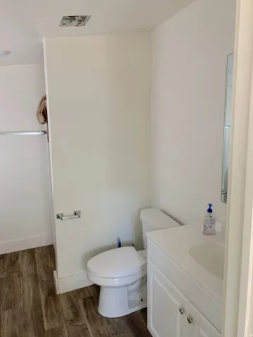 Bathroom featuring a white vanity with an integrated sink, polished chrome fixtures, wood-finish flooring, and a white commode