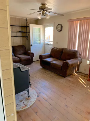 Living area featuring wood-finish flooring, a ceiling fan with integrated lighting, a built-in wall shelf system, and a door with a glass panel