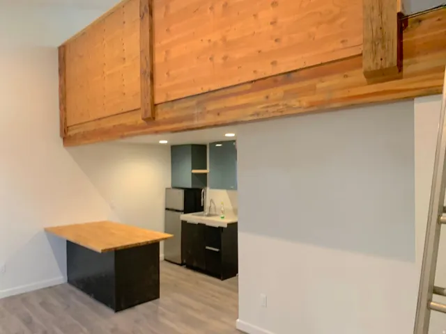 Loft-style living area featuring a built-in wood-finish table with a dark base, wood-finish flooring, and exposed timber beams