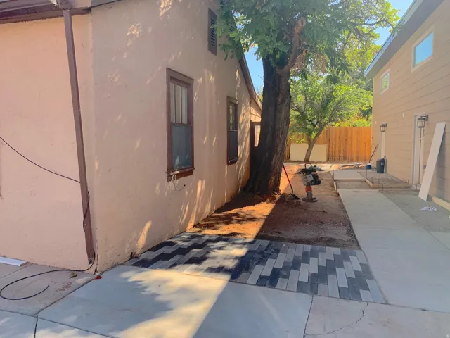 Stucco exterior with wood-framed windows, a mature tree, concrete pathways, and a paver stone patio area