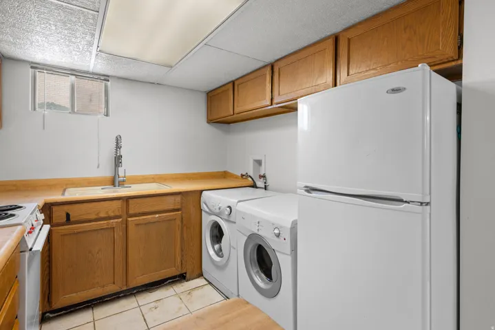 Utility area featuring light wood-finish cabinetry, a drop-in sink with a gooseneck faucet, a side-by-side washer and dryer, and a white refrigerator
