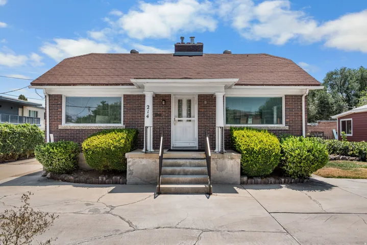 Brick exterior with a brown shingle roof, featuring a covered entryway with white columns and a white front door