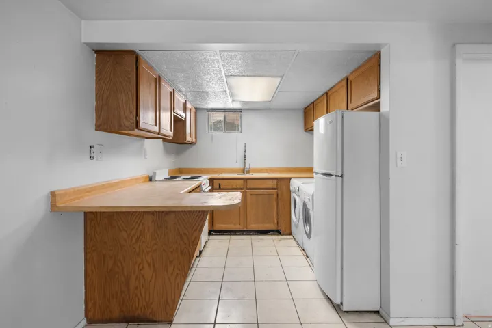 Kitchenette featuring wood-finish cabinetry, a built-in breakfast bar, tile flooring, and a drop ceiling with integrated lighting