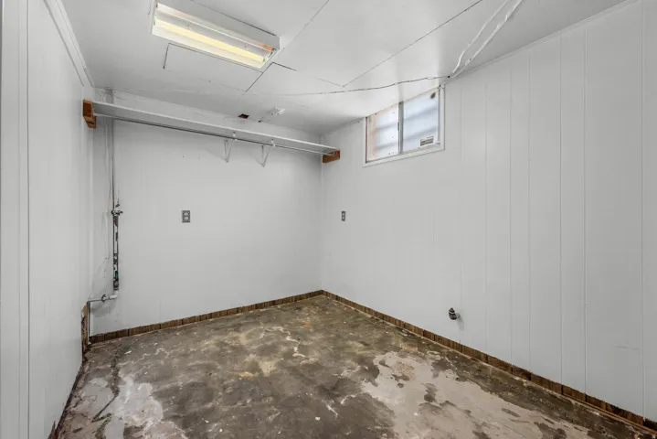 Utility space featuring concrete flooring, white paneled walls, and overhead fluorescent lighting