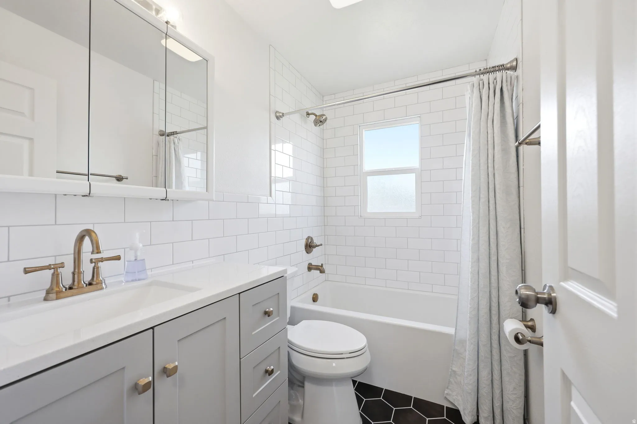 Bathroom featuring white subway tile walls, a light gray vanity with a white countertop, an integrated sink, and bronze-finish fixtures