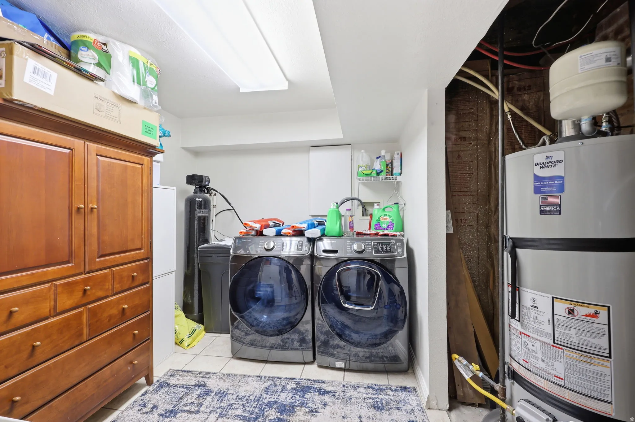 Tiled utility space featuring a water heater, water softener system, and fluorescent overhead lighting
