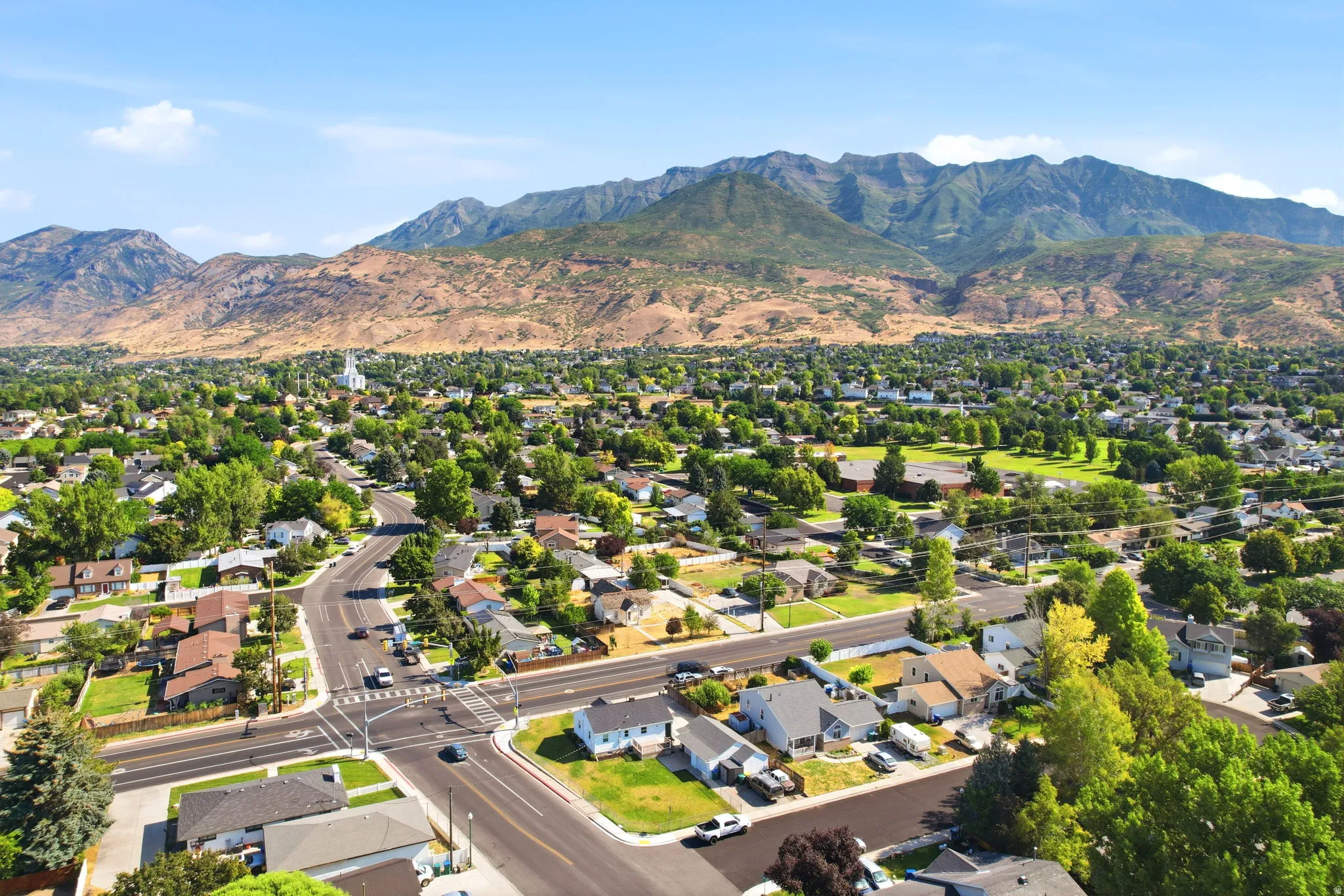Expansive aerial perspective showcasing a residential area with varied housing styles and mature trees, set against a prominent mountain backdrop