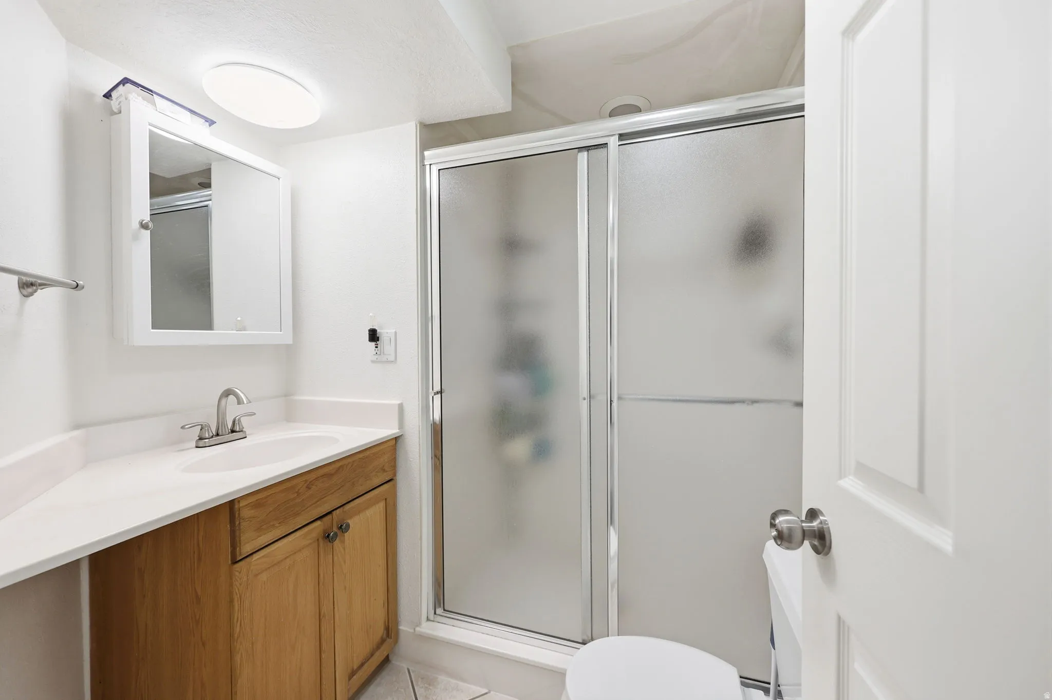 Bathroom with a light wood-finish vanity, white countertop, and integrated sink