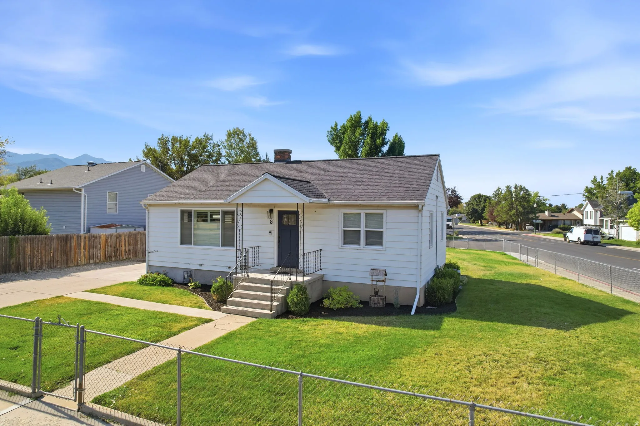 White exterior residence featuring a dark gray front door, concrete steps with metal railings, a manicured front lawn, and a paved driveway