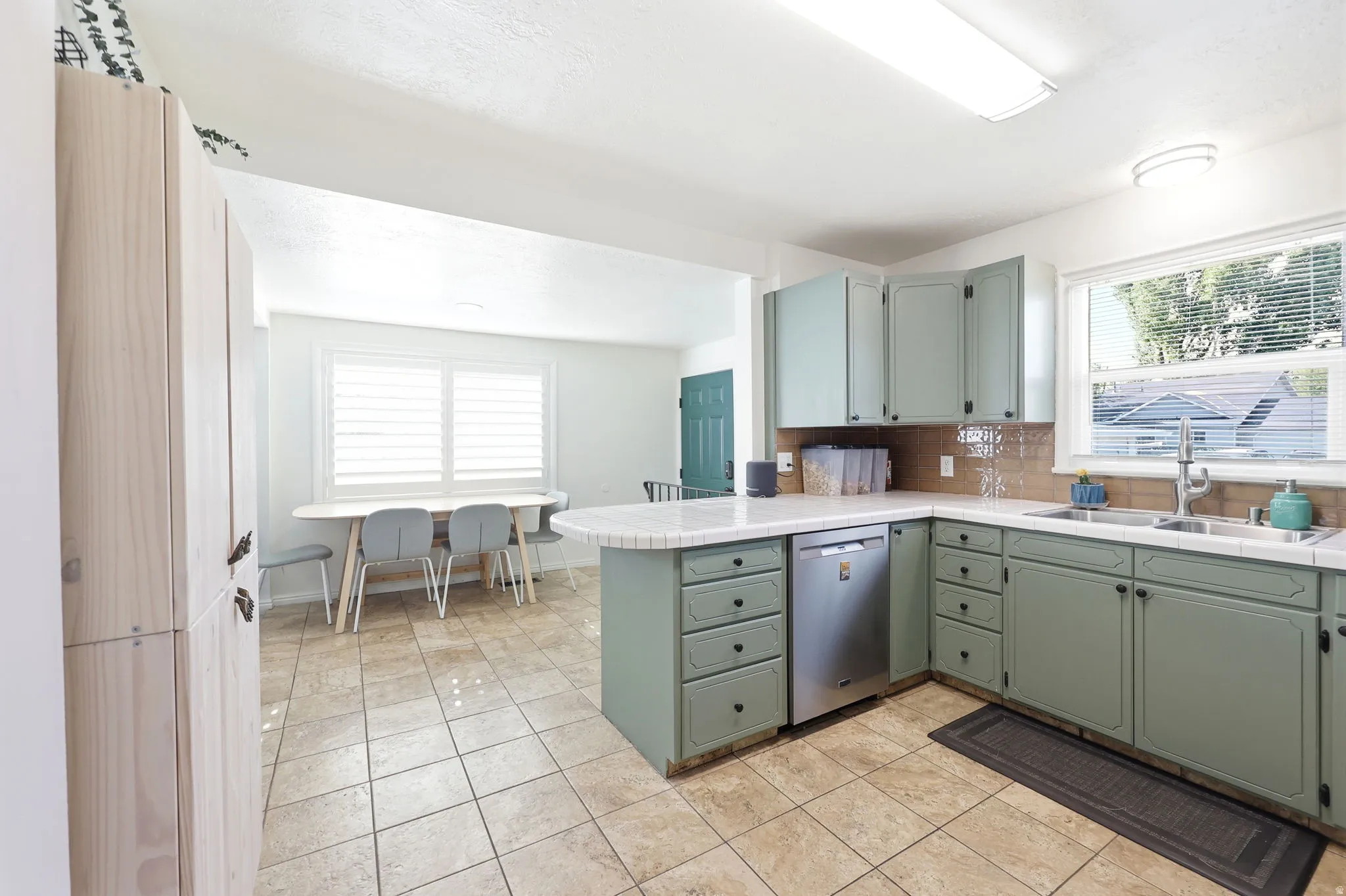 Kitchen featuring sage green cabinetry, a double basin stainless steel sink, a stainless steel dishwasher, and a light-colored countertop