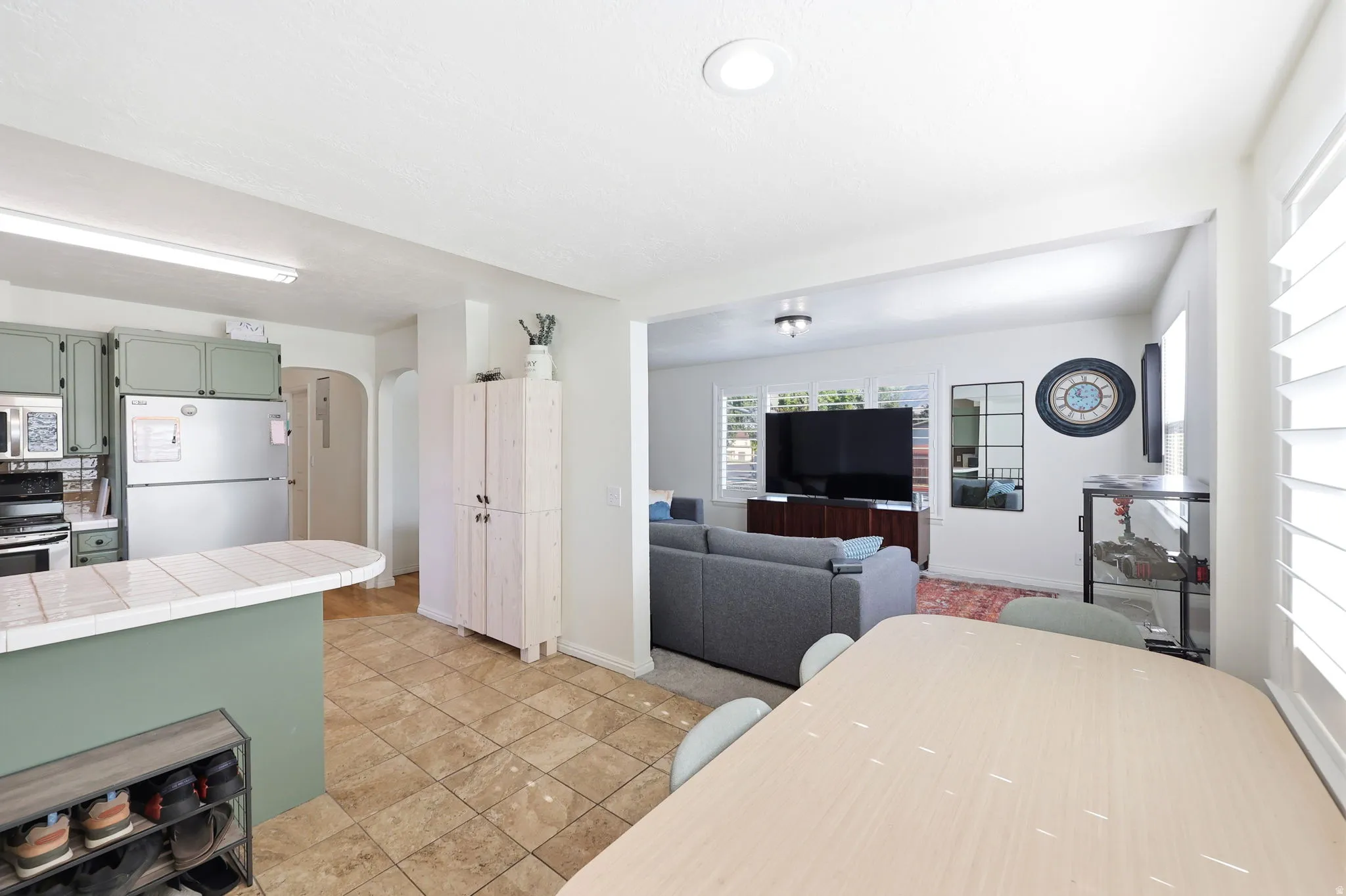 Open-concept living space featuring a kitchen with sage green cabinetry and a tiled breakfast bar, tile flooring, and white plantation shutters