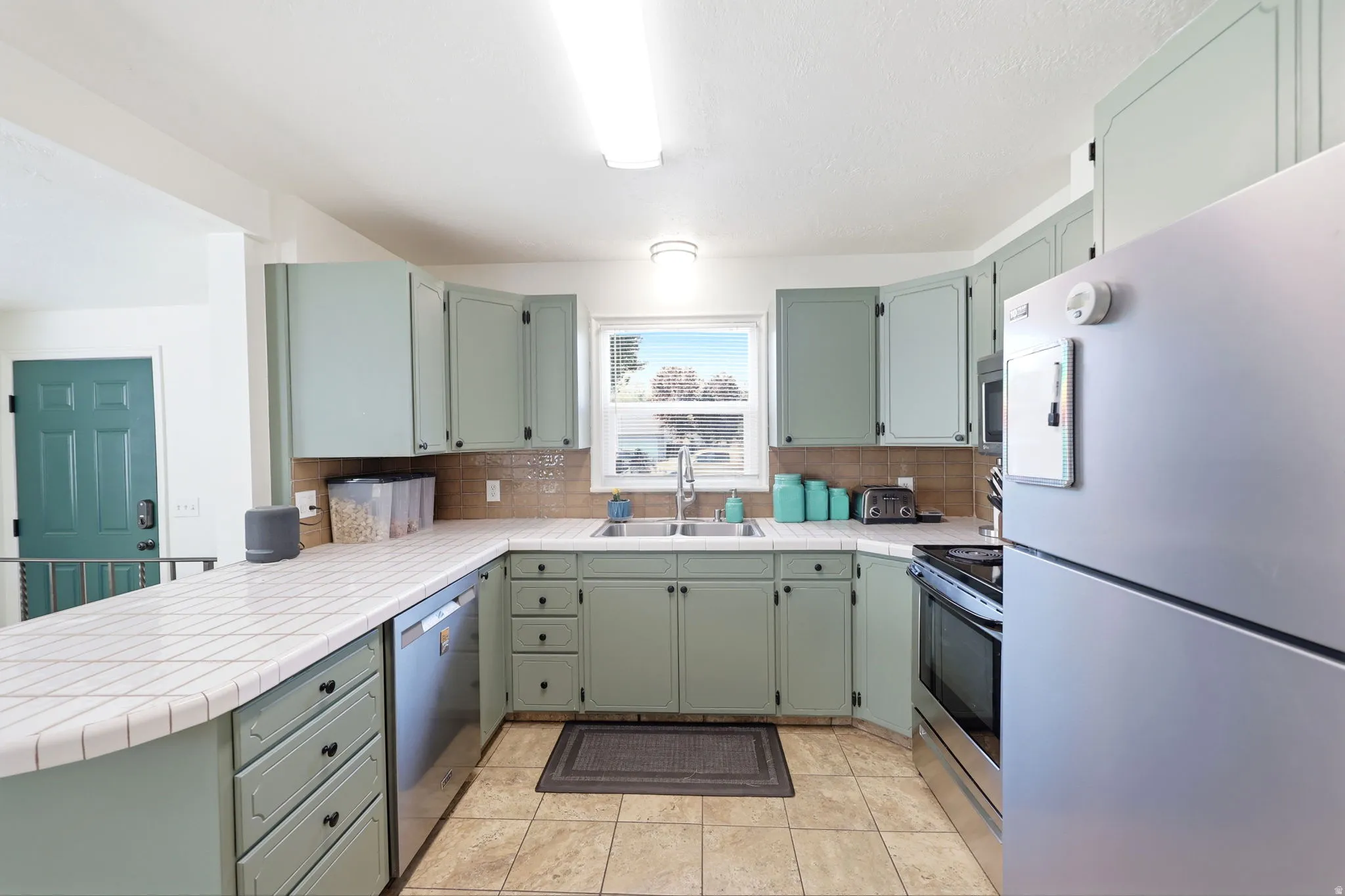 Kitchen featuring light green cabinetry, white tiled countertops, and a tiled backsplash