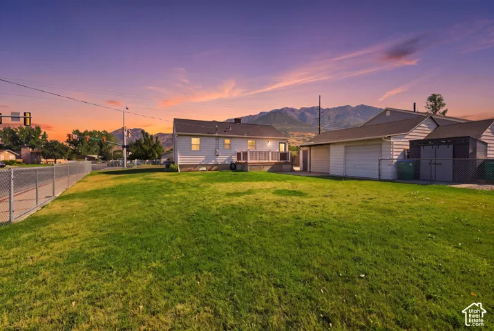Expansive lawn area featuring a chain-link fence, a detached garage, and a rear deck