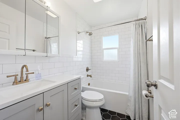 Bathroom featuring white subway tile walls, a light gray vanity with a white countertop, an integrated sink, and bronze-finish fixtures