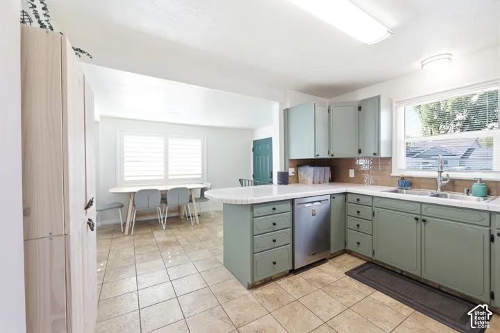 Kitchen featuring sage green cabinetry, a double basin stainless steel sink, a stainless steel dishwasher, and a light-colored countertop